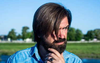 Bıyıklı vahşi sakallı adam şık bir saç kesimi ve açık havada günlük gömlek giyiyor, yaz mevsimi.