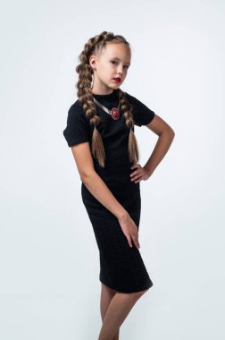 Tarzına bağlı. Geçmişi olan neşeli kız beyazda izole edilmiş görünüyor. Çocuk modası. Elbiseli bir çocuk ve saçları örgülü. Güzellik ve moda. Kuaför kuaförlüğü. çocukluk mutluluğu