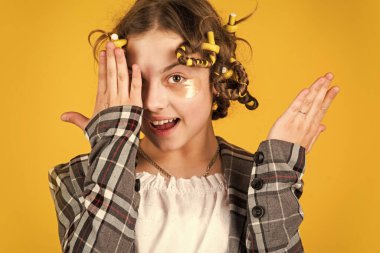 Gözlerinin altında yamalar olan sevimli bir çocuk. Çocuk manken konsepti. Çocuk saç stili yapıyor. Saçları bukleli küçük mutlu kız. Güzellik için göz altı kumaş maskesi. Ne kadar işe yaradı..