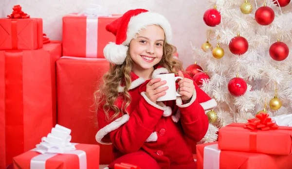 Gorące kakao w Wigilię. Ulubiony napój kakaowy. Kapelusz Mikołaja lubi napój kakaowy. Idealny sposób, aby ogrzać Ci sezon wakacyjny. Dziewczyna mało słodkie dziecko trzymać kubek z gorącym napojem podczas świętowania Bożego Narodzenia — Zdjęcie stockowe