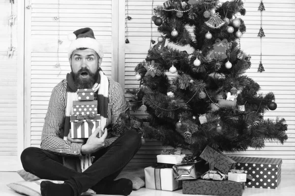 Guy en chapeau et écharpe par arbre de Noël et cadeaux. — Photo