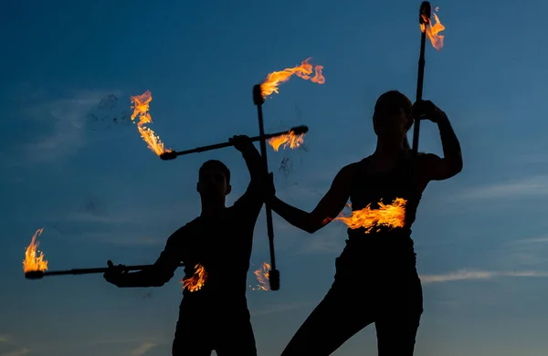 Meydan okumaya yükselin. Seksi çift yanan çubukları manipüle ediyor. Karanlık siluetler gökyüzünde ateş çubukları çeviriyor. Sopa çevirme. Yangın gösterisi. Açık hava festivali. Gece partisi. Ateş ve duman — Stok fotoğraf