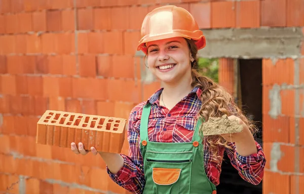 보조. 아이가 건설을 한다. 십 대 엔지니어는 건설 노동자입니다. 전문적 인 장인이나 노동자. 국제 노동자의 날. 헬멧을 쓴 소녀는 벽돌을 가지고 건축가 역할을 합니다. 집을 짓는 모습 — 스톡 사진