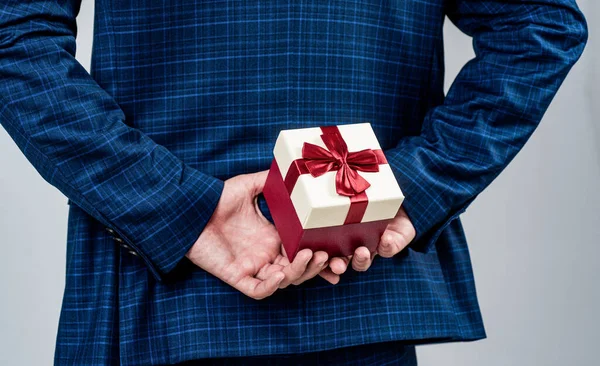 Caja de regalo atada con lazo de cinta roja sostenida en manos masculinas detrás de la espalda en traje de moda de estilo formal, día de boxeo — Foto de Stock