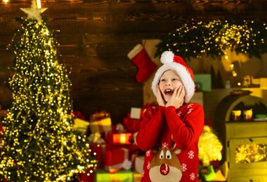 Beklenmedik bir sürpriz. Şaşırmış çocuk Noel 'i dekore edilmiş evde kutluyor. Şapkalı ve kazaklı Noel Baba çocuk. Kış Noel tatili. Hediyeler ve hediyeler. Mevsimlik alışveriş. Küçük çocuk yeni yıl partisine hazır.
