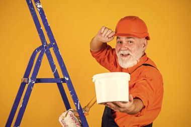 Kıdemli boyacı merdivende paten kullanır. Duvarı sarıya boyamak. İş kıyafetleri içinde profesyonel bir ressam. Odada duvar boyama işçisi. Erkek dekoratör tekerlekli sandalyeyle resim yapıyor. seçici odak