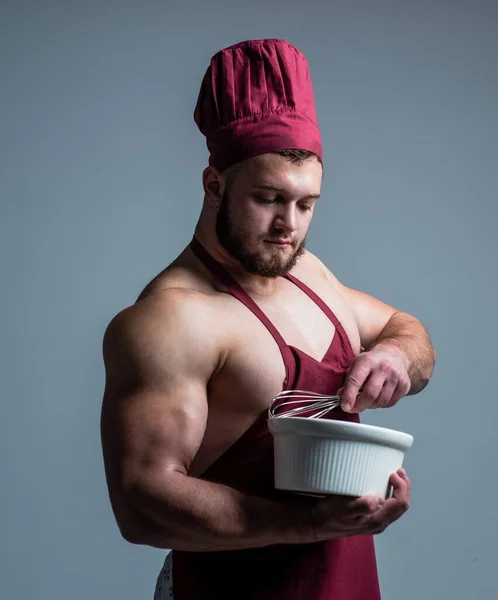 Muskularny człowiek gotować w fartuchu szefa trzymać talerz i beater, przygotowywanie żywności — Zdjęcie stockowe