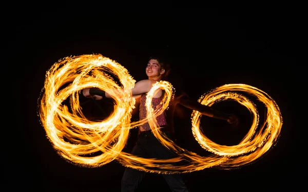 Happy male fire dancer twirl burning baton creating sparkling trails in motion dark outdoors, twirler