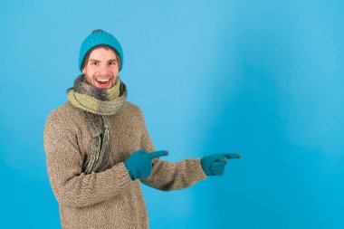 Kış satışı için ürünler. Mutlu adam bir şeyi işaret ediyor. Ürün sunan yakışıklı bir adam. Yeni ürün. Ürün tanıtımı. Reklam metni için mavi arkaplan, kopyalama alanı