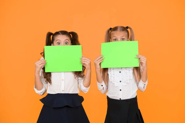 Wow. Little girls holding empty sheets of paper on yellow background. Small children with blank green school paper for assignment or project work. Examination paper. Academic paper, copy space — Stock Photo, Image