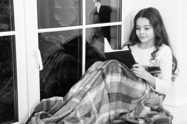 Унесена в мир фантазий. Маленькая девочка читала фантастическую книгу на подоконнике. Маленькому ребенку нравится читать сказки. Дети фантазии и воображения. Сказка. Читайте до глубокой ночи — стоковое фото