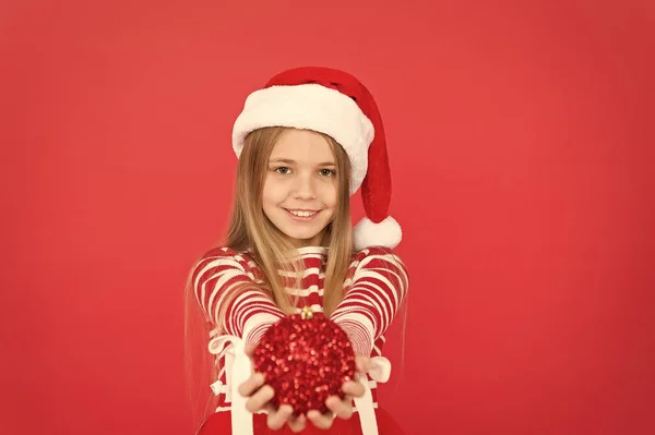 クリスマスシーズンだ。幸せな子供はクリスマスツリーボールを保持します。夏の衣装を着た女の子の笑顔赤の背景。メリー・クスマスだ。クリスマス・イブ。新年の輝き — ストック写真