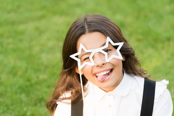 Весела щаслива дитина викладає язик в окулярах у формі зірки шкільний партійний аксесуар для святкування на зеленій траві, дитячий день — стокове фото