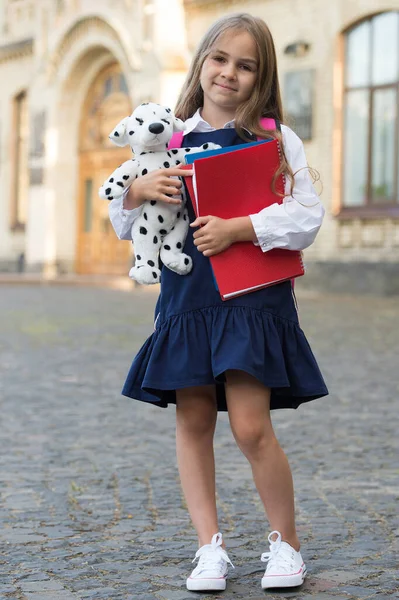 Glad liten unge i skoluniform hålla läroböcker och leksak hund utomhus, September 1 — Stockfoto