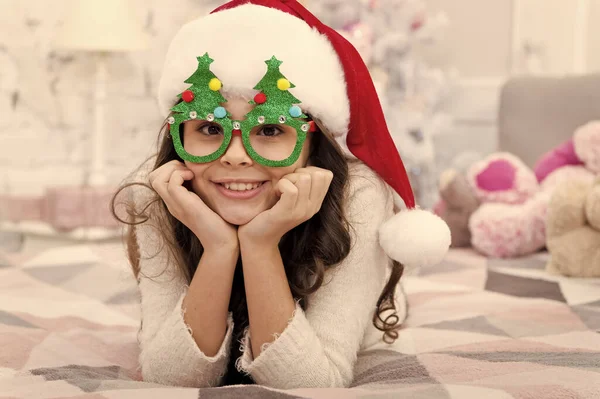 Happy new year. Wish list. Holidays atmosphere. Christmas spirit. New year holiday. Small child wear santa hat celebrate new year at home decorated interior background. Girl kid in bedroom with toys