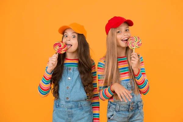 Lamiendo. Niñas disfrutando de delicioso sabor de piruletas sobre fondo amarillo. Niños pequeños lamiendo caramelos con sabor clásico a fruta. Sabe tan bien. Sabor dulce de la infancia — Foto de Stock