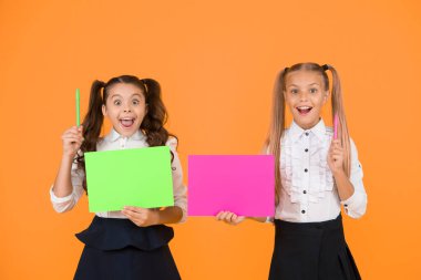 Dahi okul ipuçları. Küçük öğrencilerin fikirleri var. Küçük kızlar ellerinde kalem ve sarı arka planda kağıt tutuyorlar. Çalışma notları olan küçük okul çocukları. Küçük çocuklar ders için sunum oluşturuyorlar, kopyalama alanı