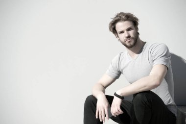 Sakallı ve günlük tişörtlü sarı saçlı adam. Maço açık havada akıllı telefon tutar. Gri duvarda cep telefonu olan sakallı bir adam. Yeni teknoloji ve modern hayat, boşluğu kopyala