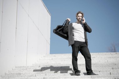 Adam mavi gökyüzündeki merdivenlerde cep telefonuyla konuşuyor.