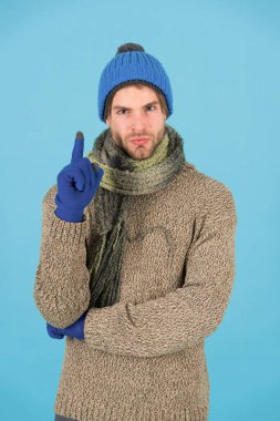 Yeni bir fikir. Tıraşsız yakışıklı adam mavi arka planda kış aksesuarları takıyor. Alışveriş konsepti. Duygusal bir ifade. Kış sezonu indirimi. Hippi, kış şapkası eşarbı ve eldiven ördü. Parmağını kaldır.
