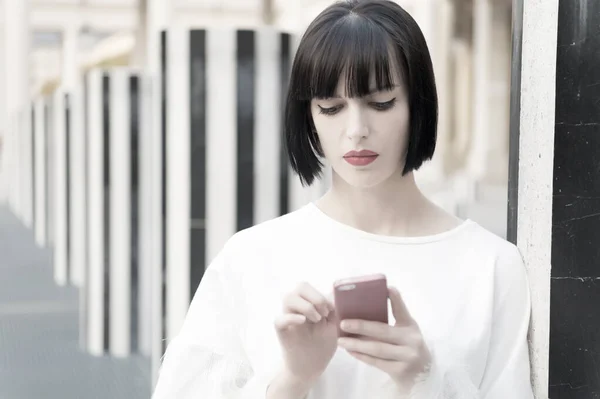 Modelo de moda com dispositivo móvel. Mulher com lábios vermelhos usar no smartphone em Paris, França. Mulher com cabelo morena segurar telefone celular. Menina de beleza com olhar sexy. Nova tecnologia para a vida moderna — Fotografia de Stock