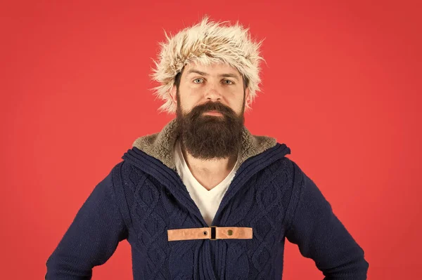 Winterherenkleding. Kleding ontwerp. Man met baard staan warme trui en hoed op rode achtergrond. Winterseizoen herenkleding. Hipster rustieke stijl harige hoed. Een modewinkel. Mannelijke kleding concept — Stockfoto