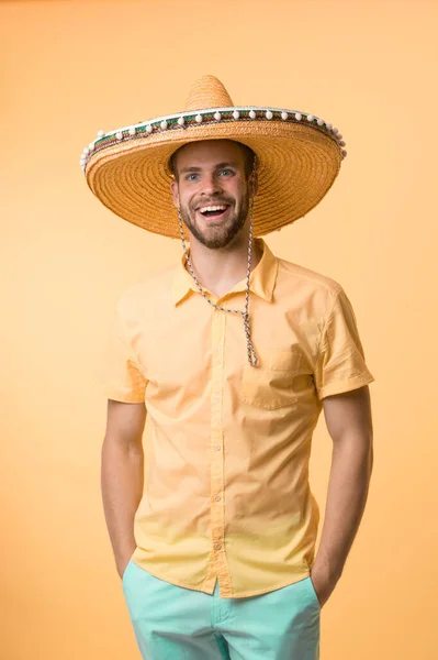 Muž na usměvavé tváři pózující v sombrero klobouku s rukama v kapsách, žluté pozadí. Chlápek se štětinatou vypadá slavnostně v sombreru. Koncept svátků a svátků. Muž ve slavnostní náladě bude slavit — Stock fotografie