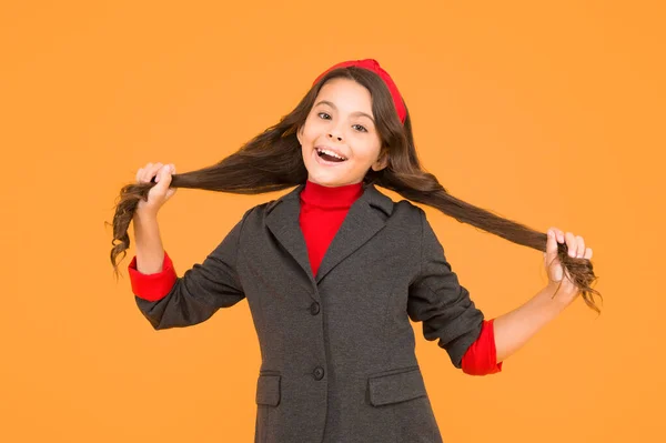 Criança pequena feliz no uniforme da escola mantenha longas travas de cabelo morena fundo amarelo, salão de beleza — Fotografia de Stock