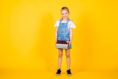 Okul tatilinde. Kitapları olan güzel bir genç kız. Çocuk okumayı seviyor. Not almak için not defteri. Çocuk edebiyatı. Okula dönüyorum. Mutlu çocukluk. Sarı arka planda sevimli bir çocuk. eğitim