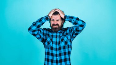 Mutsuz sakallı bir adam mavi arka planda stres hissediyor, başı ağrıyor.