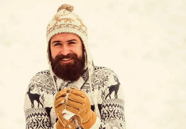 Sneeuwspelen. Veel plezier in de winter. Vrolijke bebaarde hipster gebreide muts en warme handschoenen spelen met sneeuw buiten. Kerstvakantie. Sneeuwbal maken. Geluksconcept. glimlachende man sneeuw achtergrond — Stockfoto