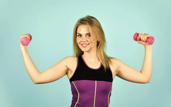 Μεγάλη πρόοδος. Λεπτή κοπέλα που κάνει τρικέφαλη άσκηση με αλτήρα στο γυμναστήριο. Προπονητής ντυμένος με αθλητικά ρούχα. μυώδης γυναίκα στην κατάρτιση άντληση των μυών των χεριών. κορίτσι χρήση barbell μπλε φόντο — Φωτογραφία Αρχείου
