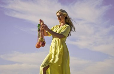 Tekrar kullanılabilir çanta. Sağlıklı yiyecekler. Sıfır atık. Elbiseli kız çanta alışverişi yapıyor. Market poşeti. Yeniden kullanılabilir eko çanta. Elinde meyve dolu bir torba tutan kadın. Bilinçli tüketim. Yankı eğilimi