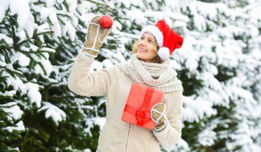 Parlak anılar. Bayan Kırmızı Noel Baba şapkası kürk ağacında. Beyaz karla kaplı kış ormanı. Açık hava mükemmel bir ruh halidir. Mutlu kadının elinde Noel hediyesi kutusu var. Noel ağacı süslemeli kız