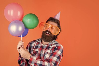 Dostça bir hizmet. Sakallı ve bıyıklı neşeli bir adam. Balonla gülümseyen hippi. Mutlu bir partiyi kutluyoruz. Parti elemanları ve tatil eşyaları. Çok renkli eğlence. Emeklilik için en iyi parti