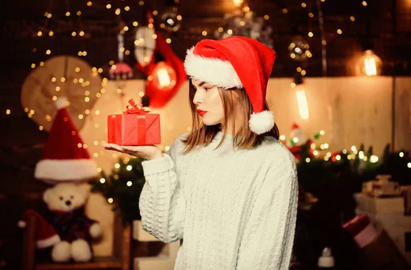 Cozy christmas atmosphere. Believe in miracle. Woman santa claus hat on christmas eve. Lady adorable face celebrate christmas at home. Open her gift. Girl stylish makeup red lips hold christmas gift — Stock Photo, Image
