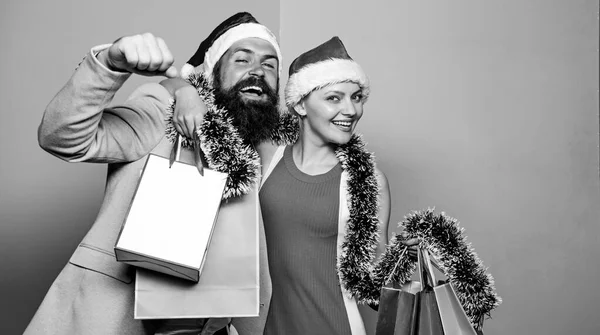 Buon Natale a tutti. Uomo e donna che fanno shopping. Shopping natalizio. Coppia allegra Babbo Natale cappelli tengono sacchetti di carta. Compra regali. Felice anno nuovo. Shopping di famiglia. Unisciti alla celebrazione. Preparare i regali in anticipo — Foto Stock