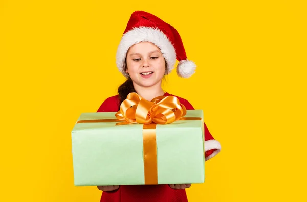 Niño mantenga presente caja de fondo amarillo. Feliz Navidad y felices fiestas. Los sueños se hacen realidad. Vacaciones de invierno. Mi feliz día. Compras de regalos de Navidad. Paquete regalo. Pequeña niña Santa sombrero celebrar caja de regalo —  Fotos de Stock