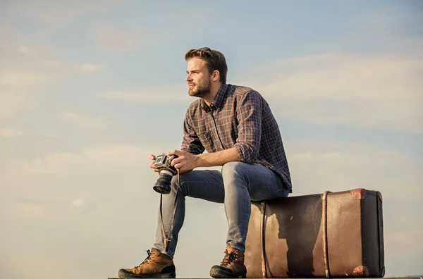 Vergessen Sie nicht zu reisen. Macho-Mann Tourist sitzt auf Reisetasche. Reisende warten auf den Flug. Bewegen. sexy Mann Himmel Hintergrund. Männermode. sieht so trendy aus. Fotograf mit Fotokamera. Geschäftsreise — Stockfoto