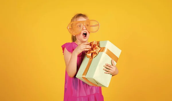 Regalo de sorpresa. su hora de compras. Niña pequeña sostiene la caja de regalo. niño pequeño con caja de regalo. Feliz fiesta de cumpleaños. felicidad infantil. Celebremos la fiesta. niño en el día de verano sobre fondo amarillo — Foto de Stock