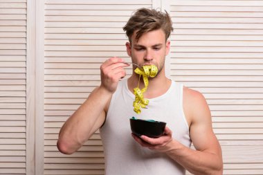 Beyaz atletli adam kıvrımlı bandı ağzına sokuyor.