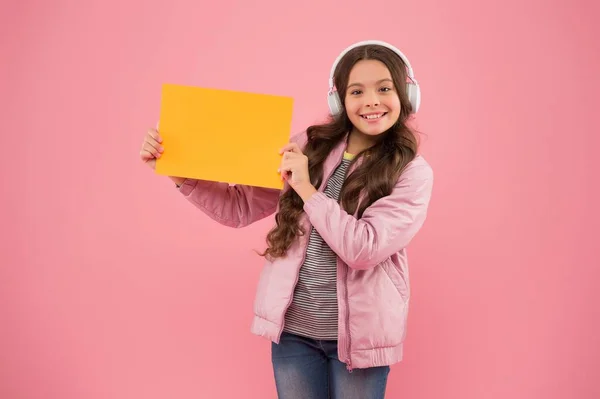 Vrolijk kind draagt oortjes en toont leeg papier voor kopieerruimte, reclame — Stockfoto