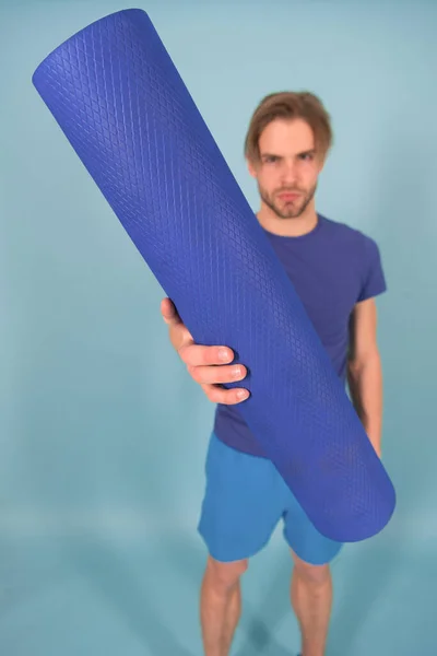 Tapete de ioga ou pilates na mão do homem borrão. Tapete azul rolou na mão. Equipamento de ginástica para treinamento e treino. Yoga ou pilates e atividade esportiva — Fotografia de Stock