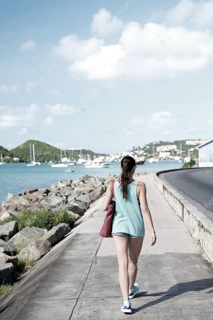 Sexy woman walk along sea in st.thomas, british virgin island. Woman in top and shorts on sea side promenade on sunny day, back view, beach fashion. Summer vacation on island, wanderlust