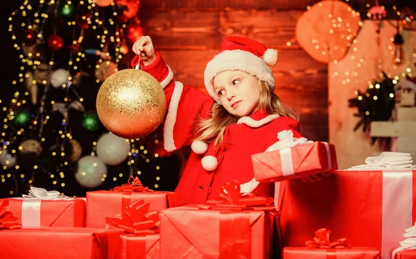 Чарівний скляний м'яч змушує її відчути унікальну атмосферу Різдва. Маленька дитина тримає різдвяний блискучий м'яч. Маленька дівчинка дивиться на кульку з орнаментом. Мила дитина з золотим різдвяним м'ячем — стокове фото