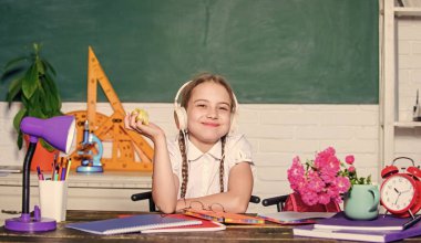 Elma meyvesi yiyen küçük bir kız. Ders aralarında atıştırmalık. Liseli kız masa başında tahtada oturuyor. Okuldaki çocuk öğrenci. Sağlıklı bir yaşam tarzı. Okul hayatı konsepti. Modern çocukluk. Okul molası