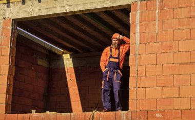 İnşaatta günlük rutin. İyi iş çıkardın. Tamirci inşaat alanında dinlenirken yoruldu. Sigara içen bir inşaatçı. Kır ve rahatla. Sakallı, mühendis üniformalı ve kasklı bir adam. Düzenli gün