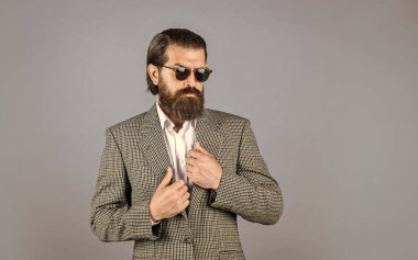 Gri arka planda duran yakışıklı adam. Ciddi sakallı iş adamı. Modern görünümlü şık, olgun bir adam. Erkek ceketi dolabı. Modaya uygun bir adam gözlük takıyor. Resmi manken. Boşluğu kopyala
