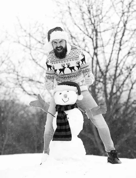 Winter games. Winter activity. Fun and entertainment. Winter vacation. Man made snowman. Hipster with beard outdoors. Man with Santa hat having fun outdoors. Guy happy face snowy nature background