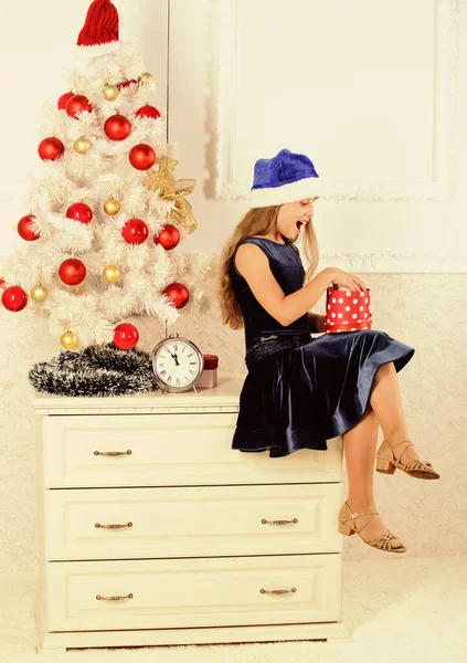 Czas otworzyć prezenty świąteczne. Szczęśliwego Nowego Roku. Dziecko świętuje święta w domu. Dziewczynka siedzi w pobliżu choinki trzymać pudełko prezentów. Mała dziewczynka Santa kapelusz podekscytowany prezentem świątecznym lub prezent — Zdjęcie stockowe